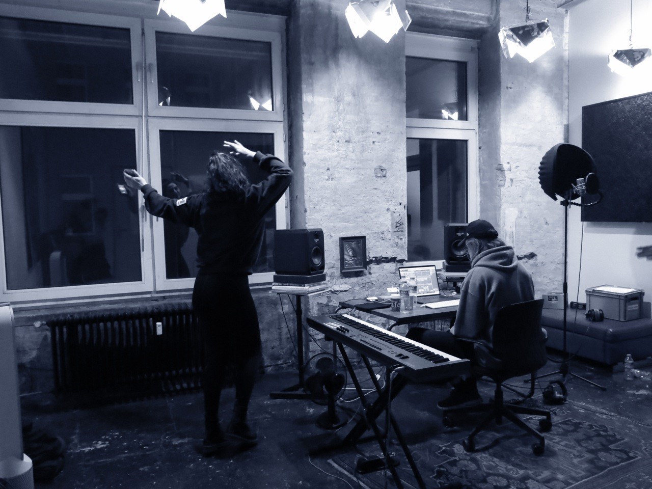 To personer beskæftiget med sangskrivning, stående foran et stort vindue i et optagestudie.