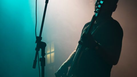 En mand, der spiller guitar i et svagt oplyst rum, søger trøst gennem musik.