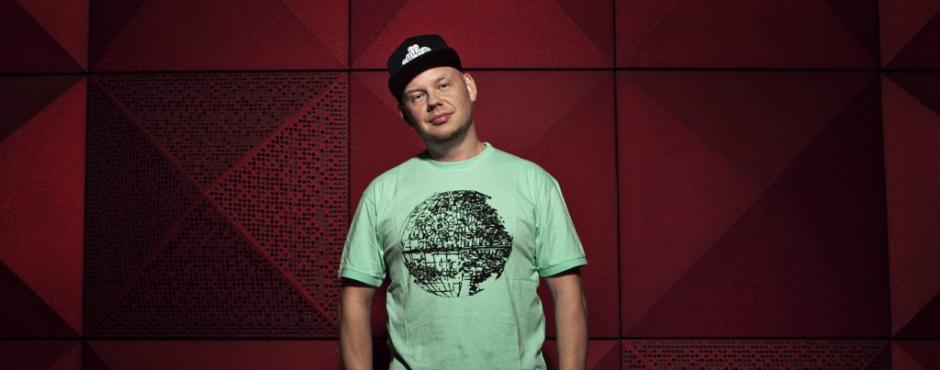 A man in a green t - shirt standing in front of a red wall.