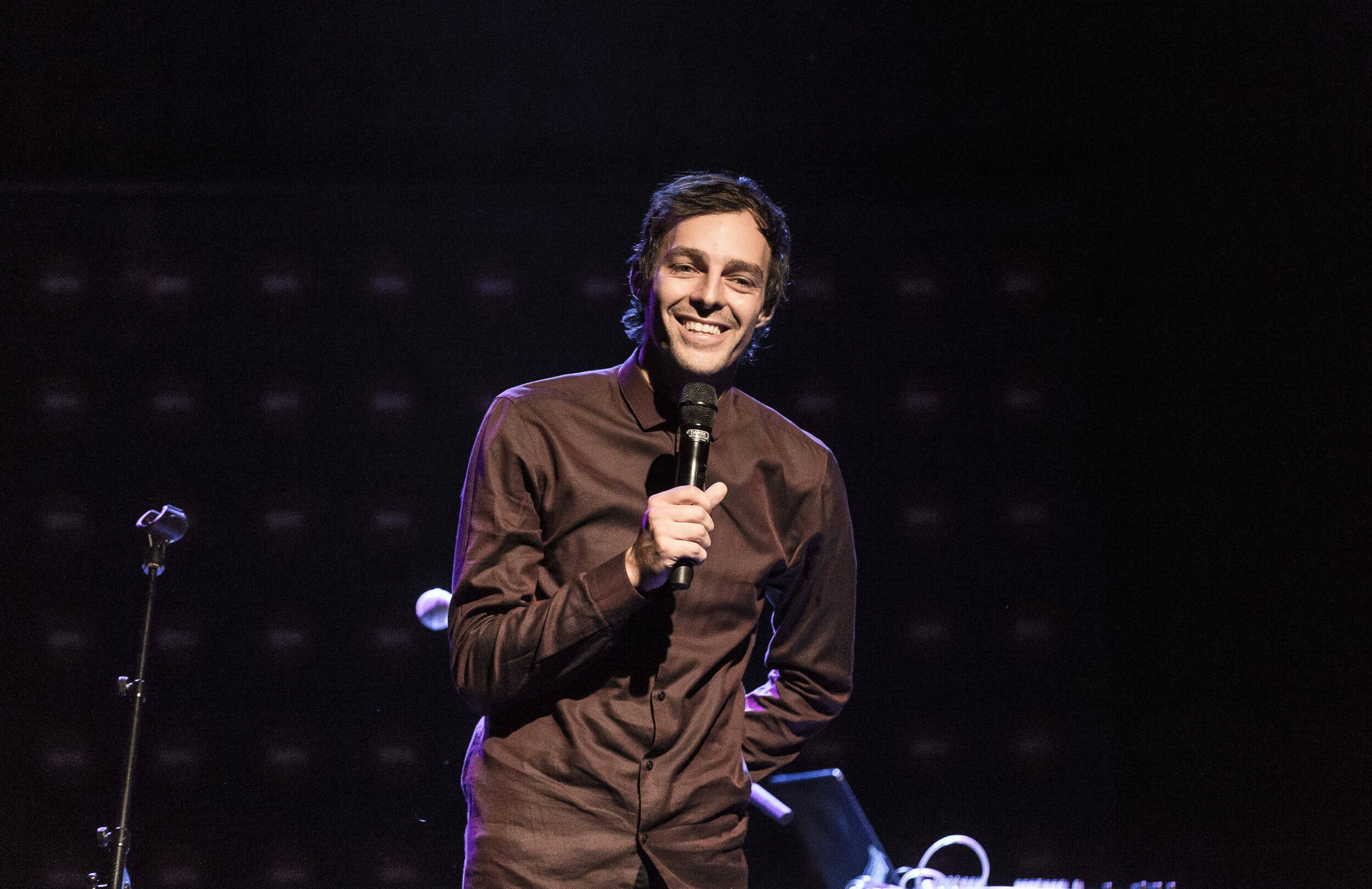 En mand i brun skjorte, der står ved siden af en mikrofon ved DJBFA's hæderspriser-arrangement 2019.