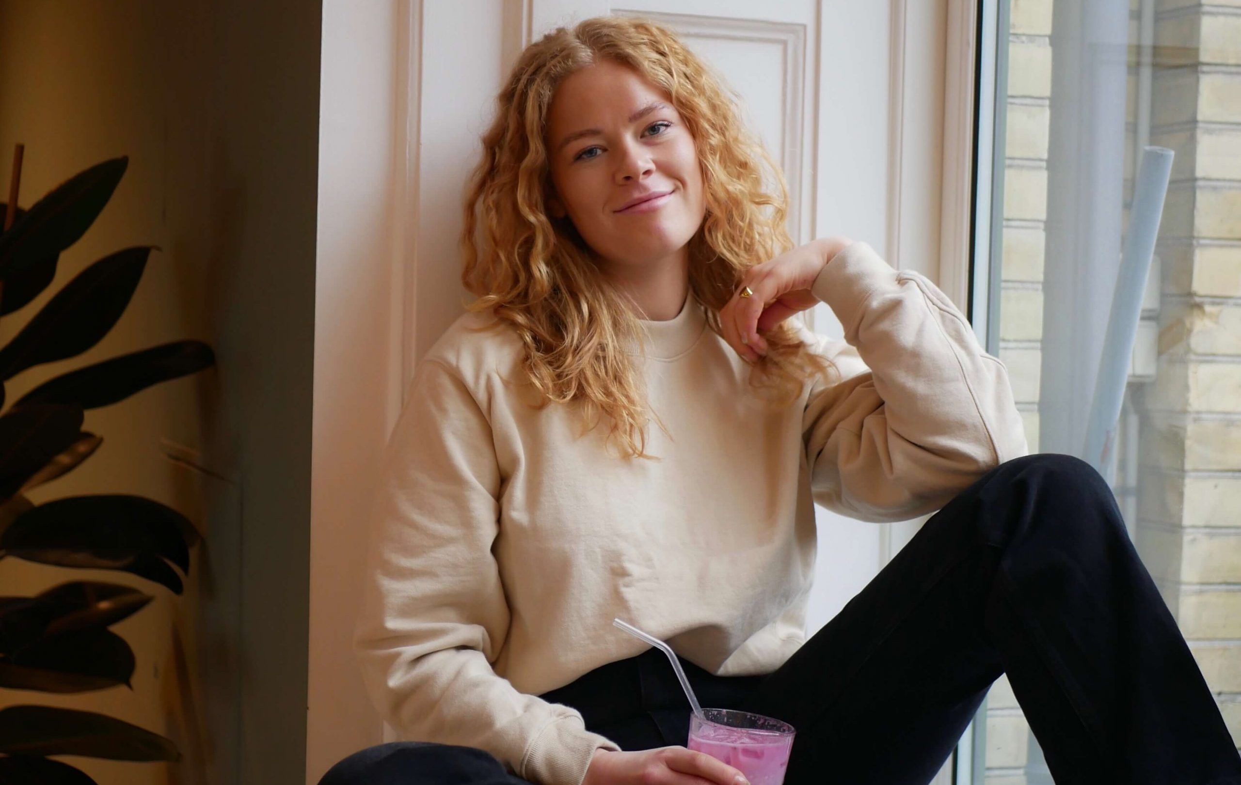 Victoria Jespersen, en kunstner underskrevet med Warner Music, sidder i en vindueskarm med en drink, mens hun er i samtale.
