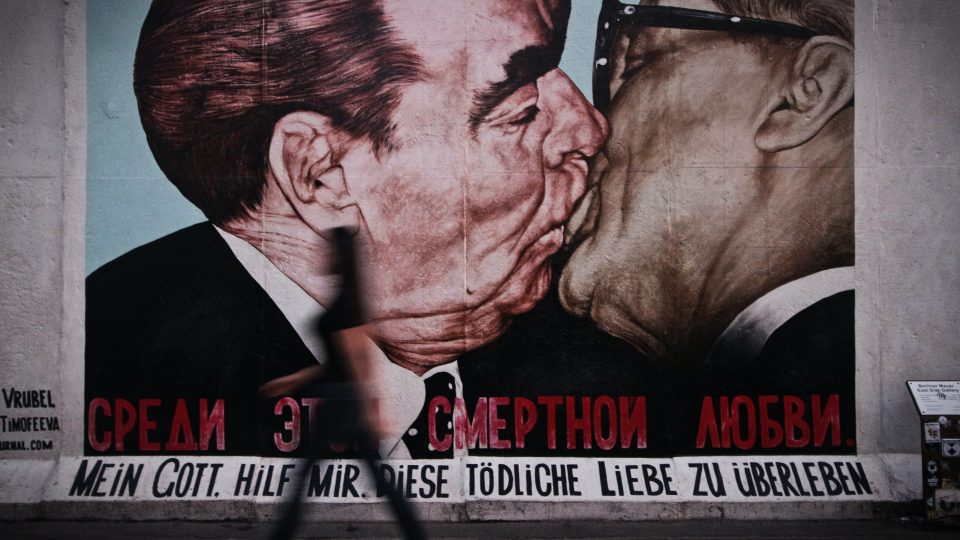En mand går forbi et vægmaleri i Berlin med en mand, der kysser en kvinde.