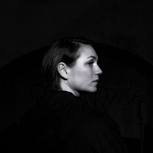 Et sort/hvidt foto af en kvinde ved navn Katrine, der står i en mørk tunnel.