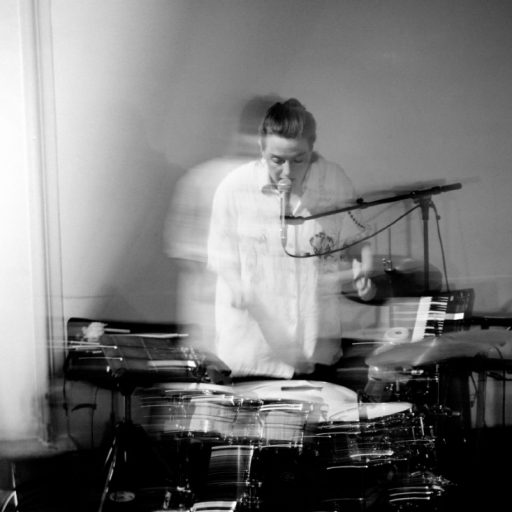 Et sort/hvid foto af en mand, der spiller trommer af Anja Jacobsen.