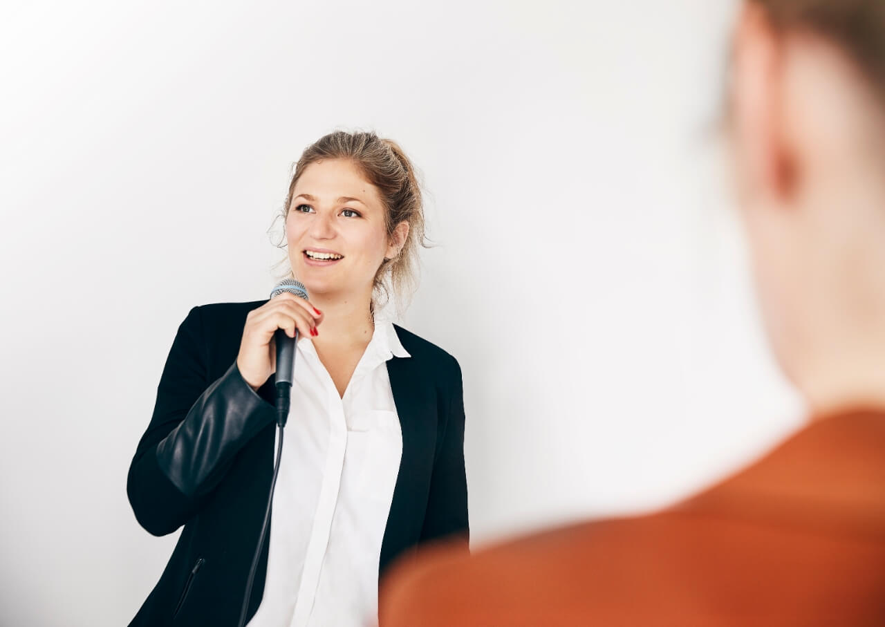 En kvinde taler i en mikrofon foran en anden kvinde.
