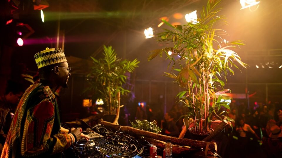 En elektronisk DJ til en fest med en plante foran sig, der skaber en fusion af Amsterdams pulserende musikscene.