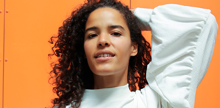 Anya poserer med sit krøllede hår foran en orange væg under en Masterclass.