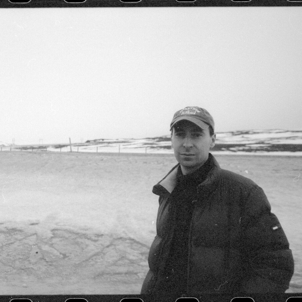 Hjalte Ross står i mørk jakke og kasket, fordybet i den fredfyldte skønhed i et snelandskab under en overskyet himmel.