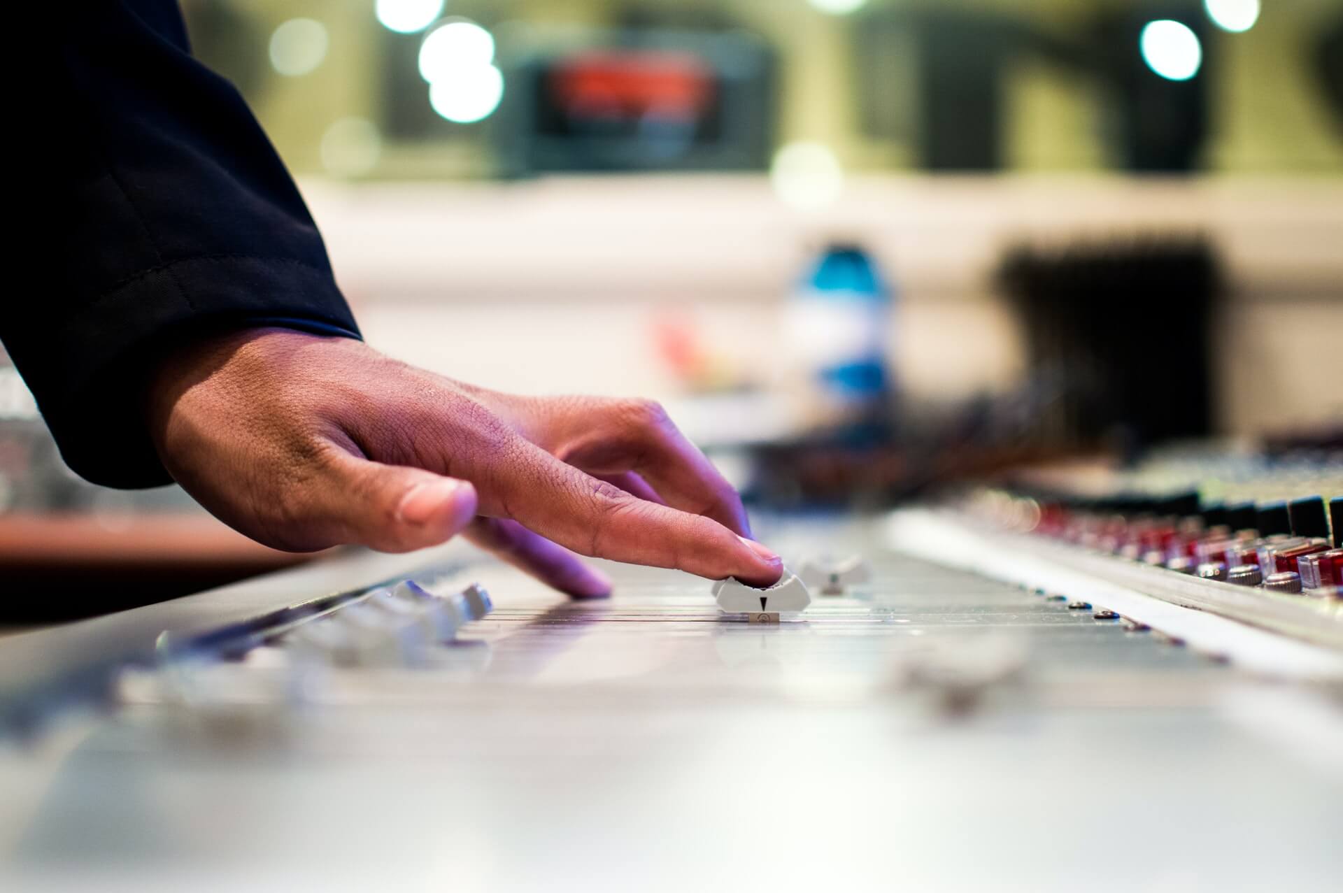 En persons hånd manøvrerer dygtigt knapper på et blandebræt under masteringsprocessen.