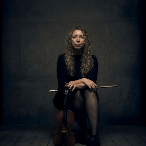 Annelene, en kvinde, der sidder på et trægulv med en violin.