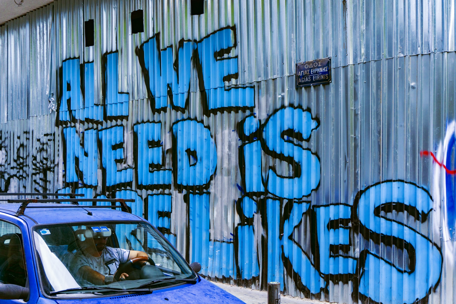 En blå bil parkeret foran en bygning med graffiti på, fanget til sociale medier.
