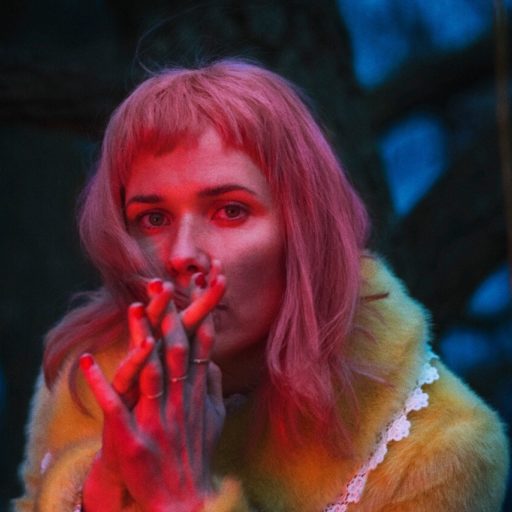 En kvinde med lyserødt hår, kendt som Oh Land, ryger en cigaret i en skov.