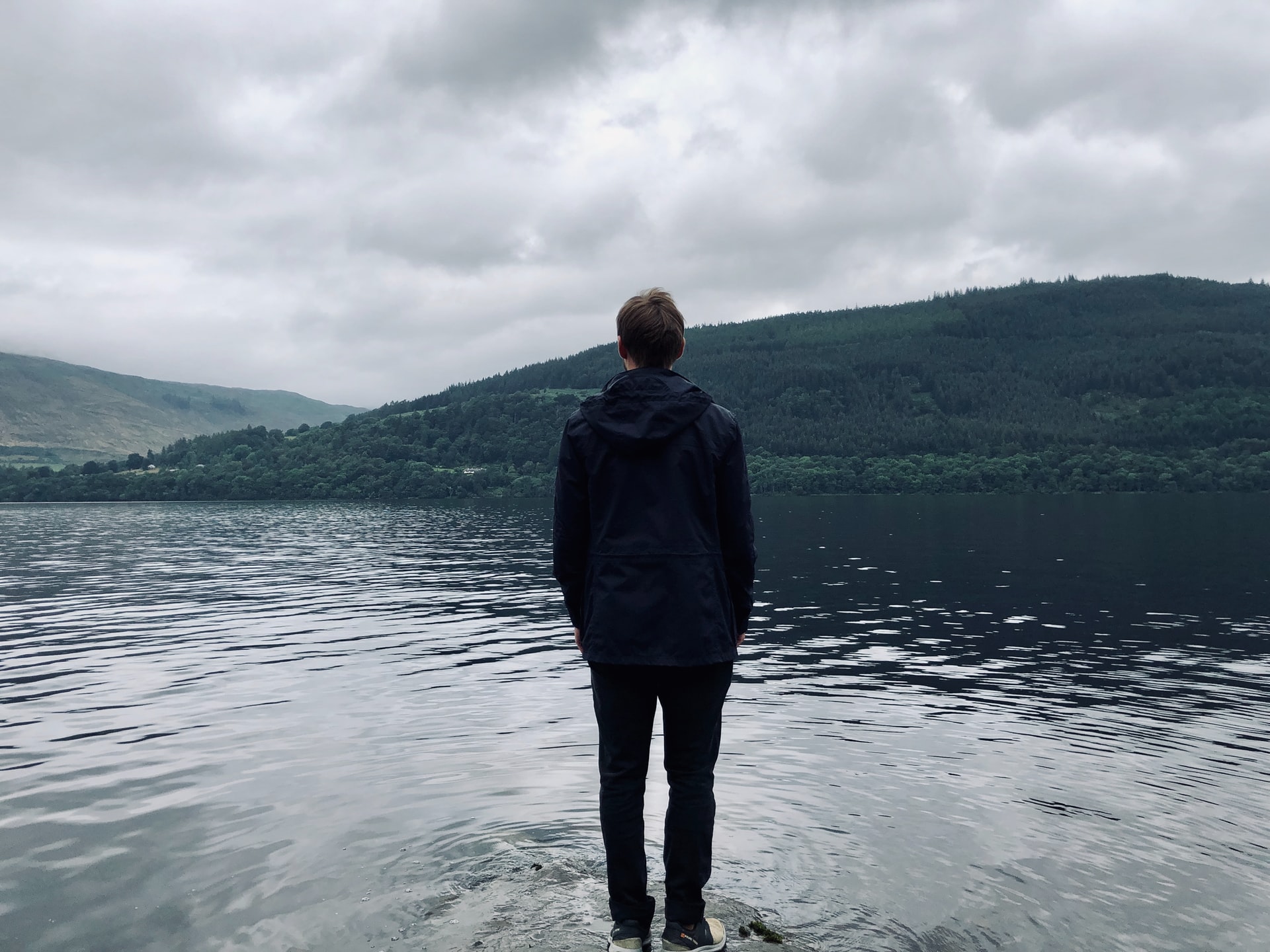 En mand, der forbedrer sit mentale velvære og styrke, mens han står på en klippe og beundrer en fredfyldt sø.