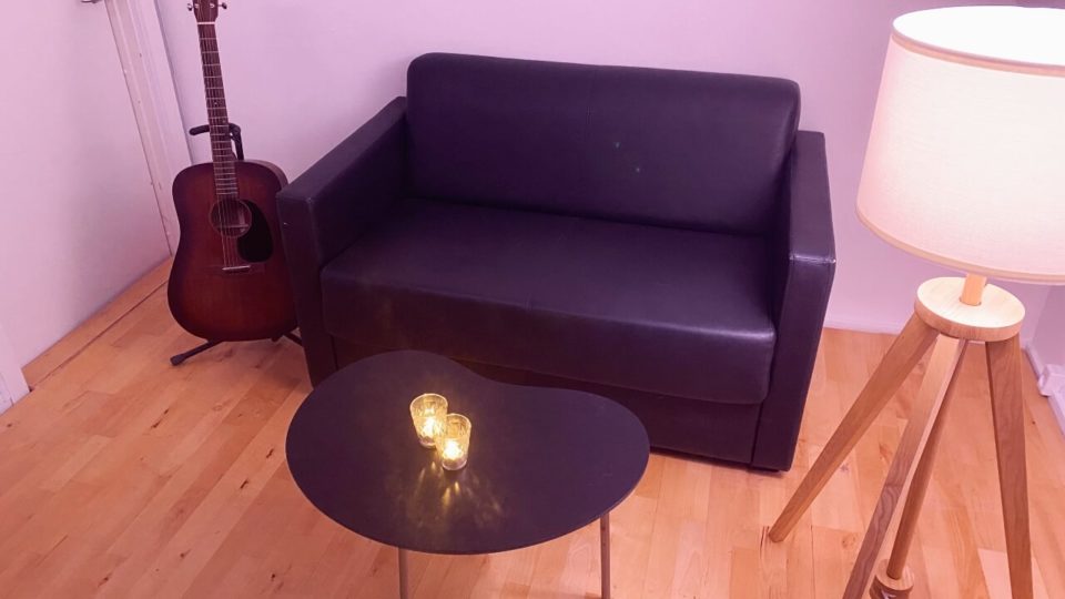En sort sofa i et københavnsk studie med en guitar og en lampe.