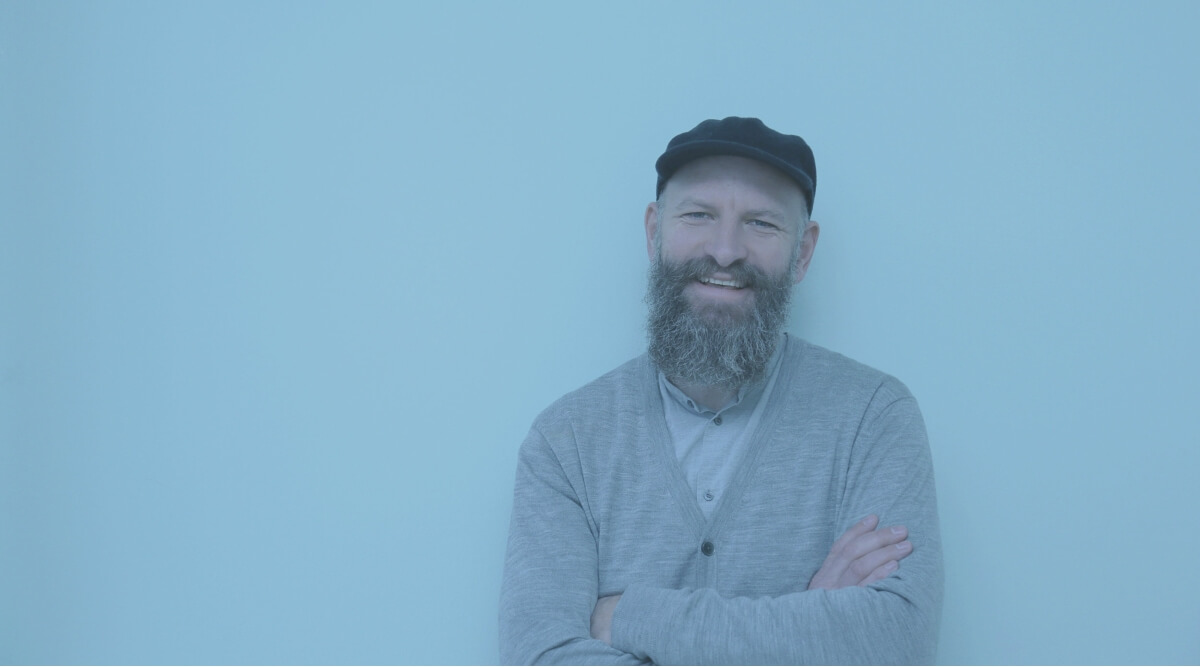 Jesper Mechlenburg, en mand med skæg, der står foran en blå mur.