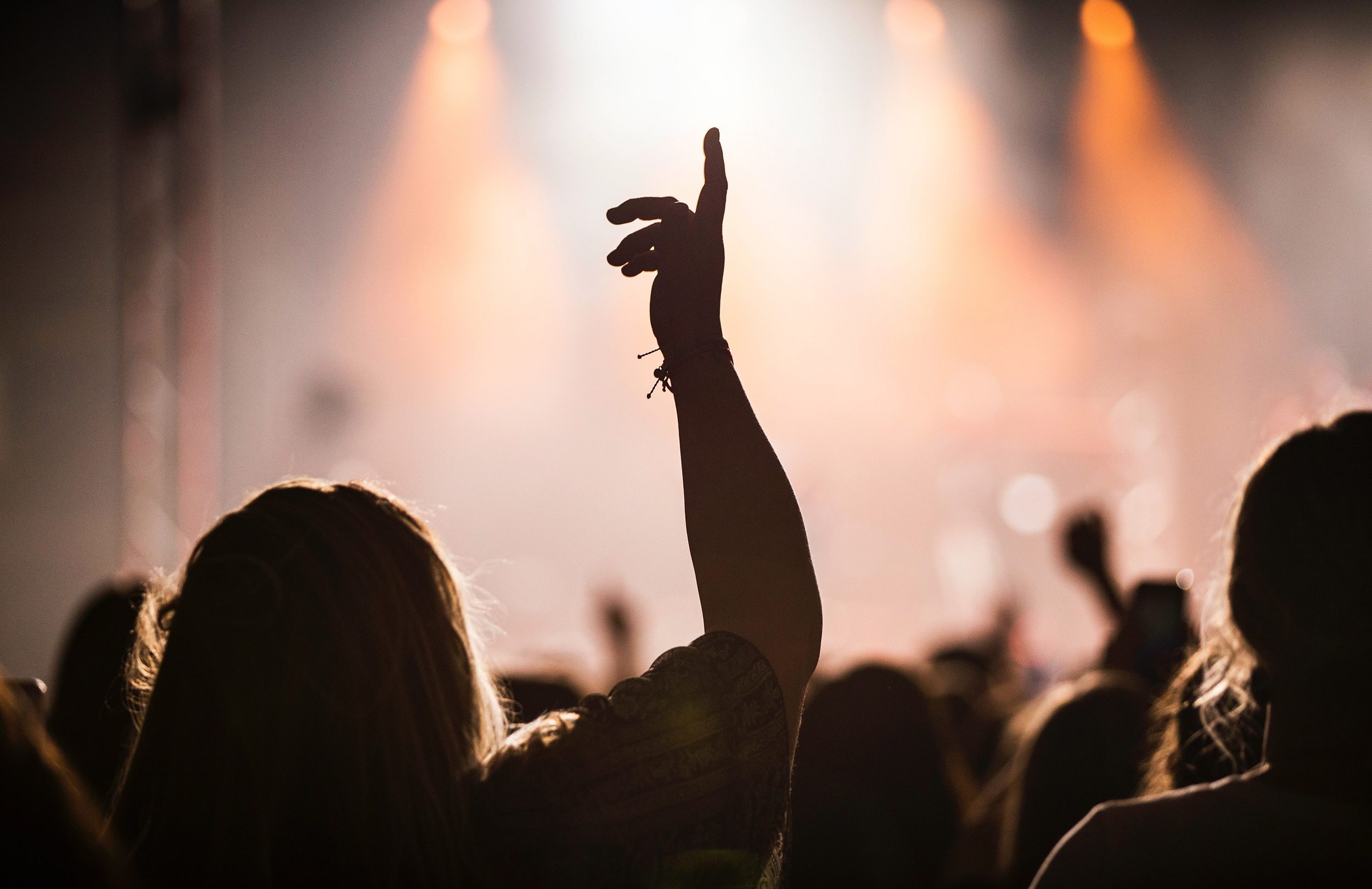 En gruppe mennesker ved en Koncertbooking løfter hænderne i vejret under en live-session.