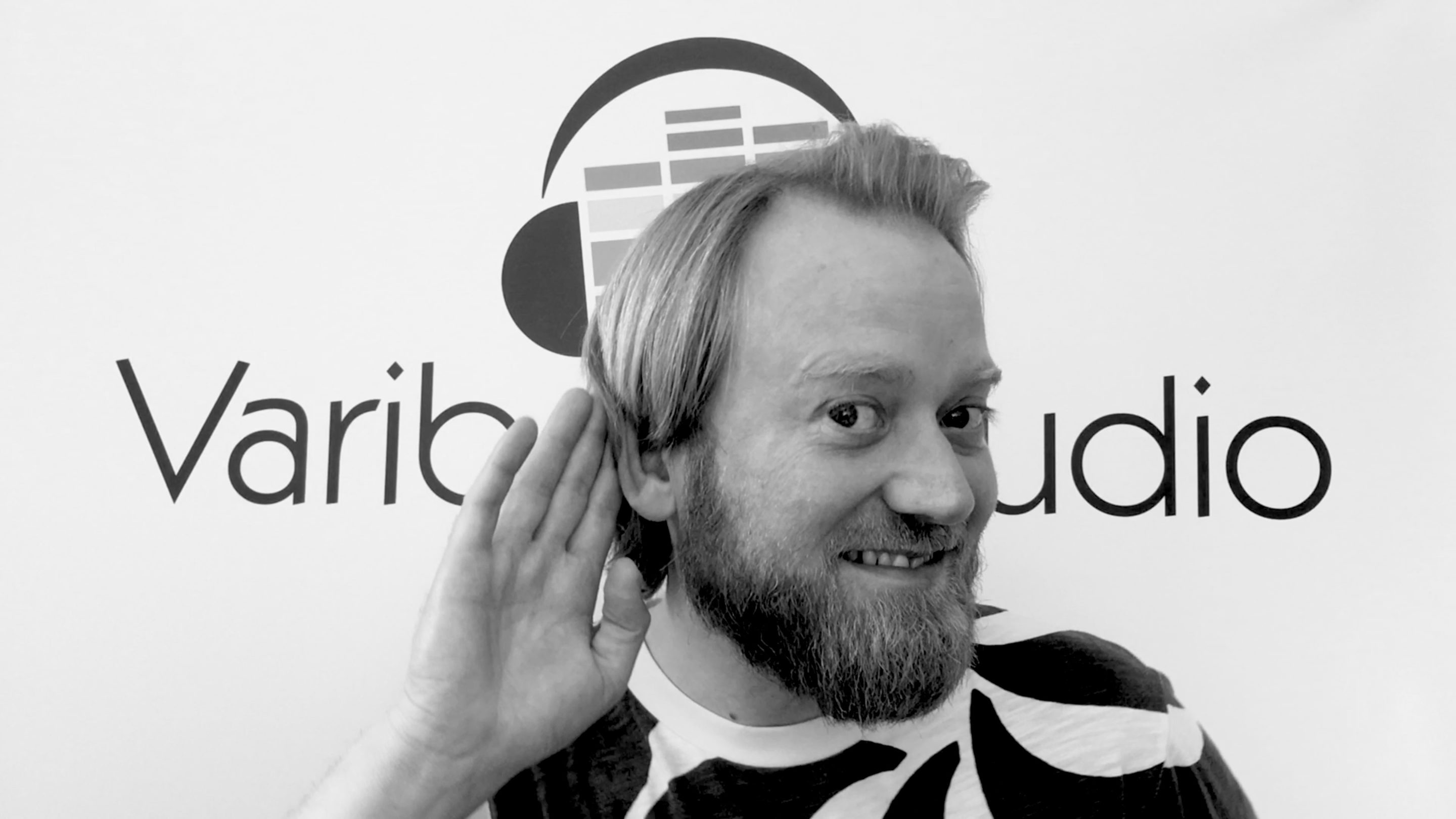 En skægget mand med hovedtelefoner foran et skilt, hvor der står Vario Studio, mastering.