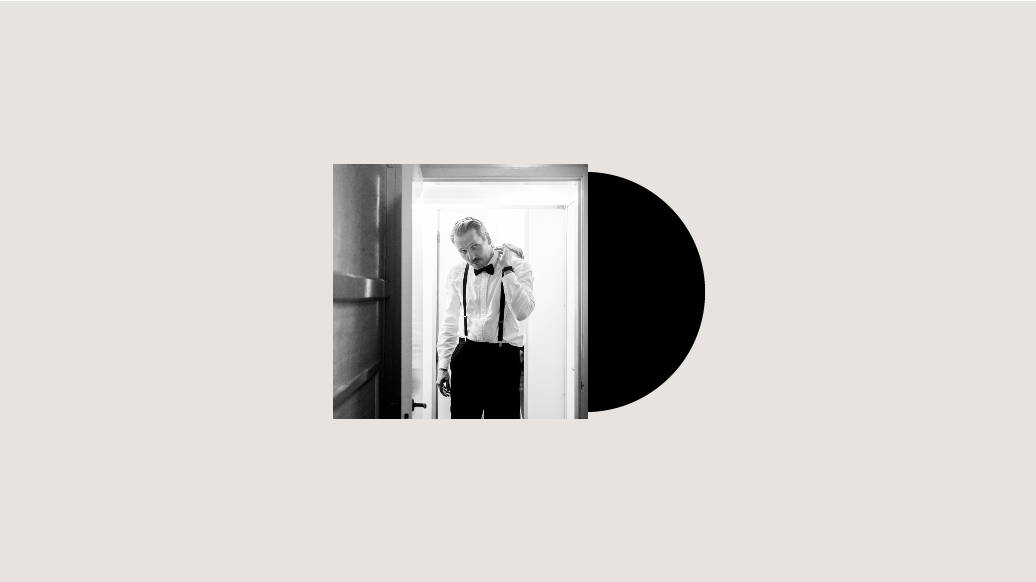 Et sort/hvidt foto af Mikkel Hess stående i en døråbning, præsenteret i en playliste.