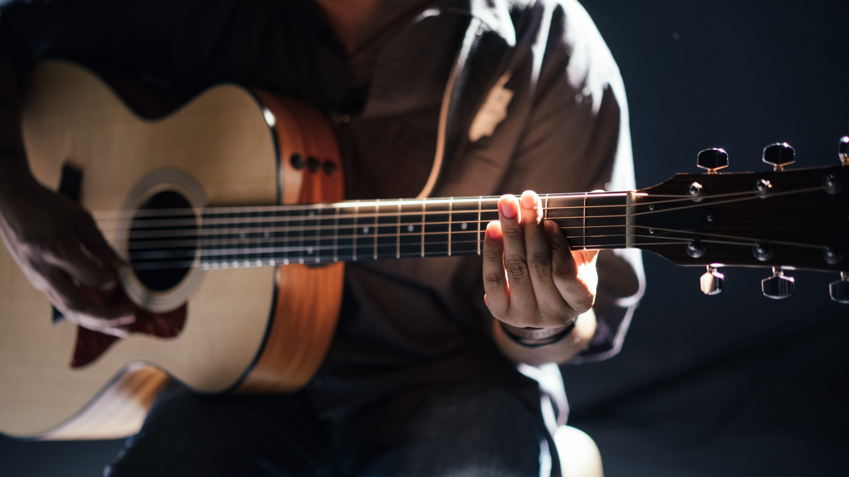 En mand, der klimprer på en akustisk guitar og viser sit musikalske talent og kreativitet som en af musikkens skabere.