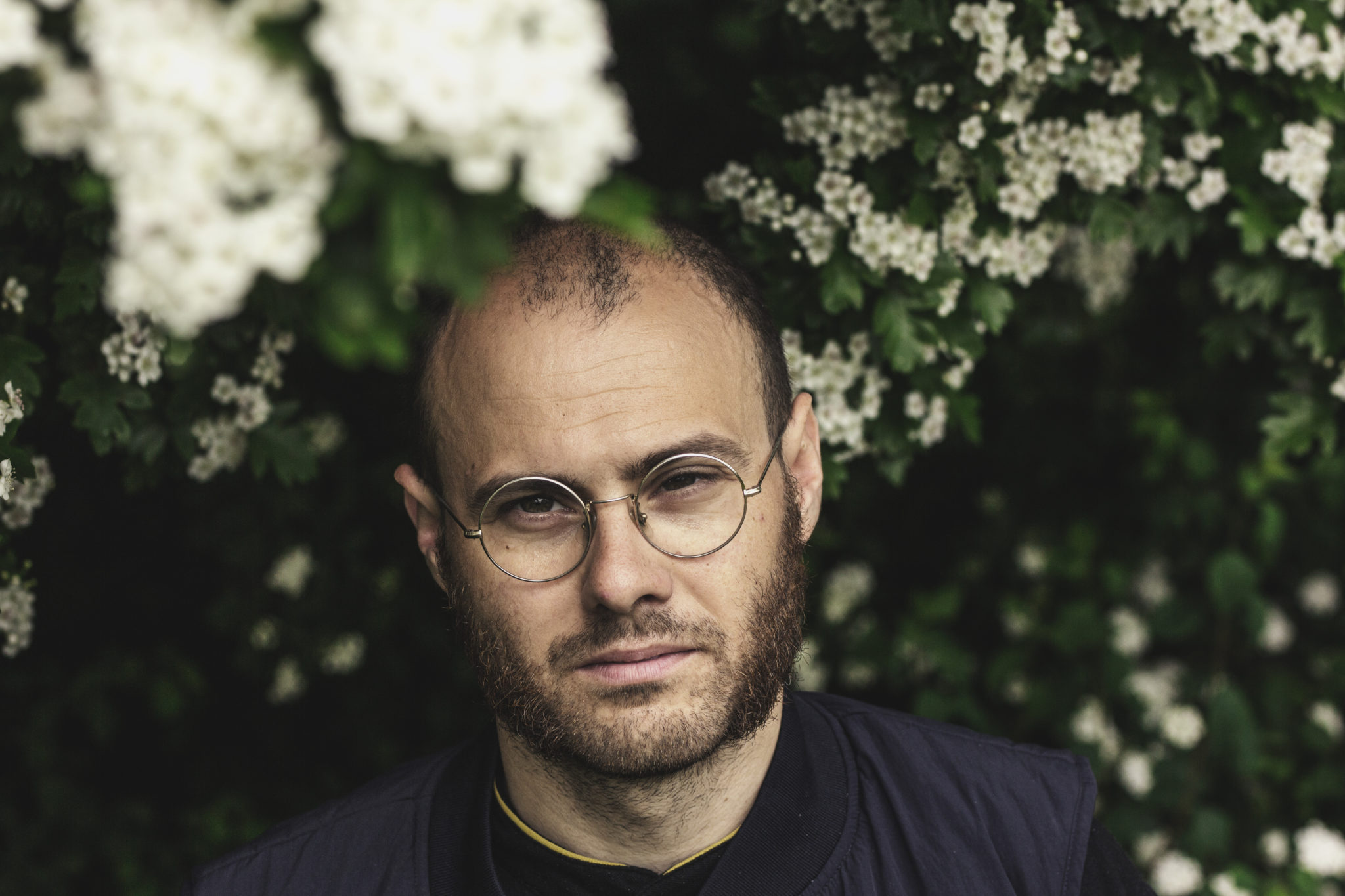 En skaldet mand i briller, som er medlem af DJBFAs medlemmer, står foran nogle blomster til PR-fotos. Han kan ses nyde landskabet, mens han poserer