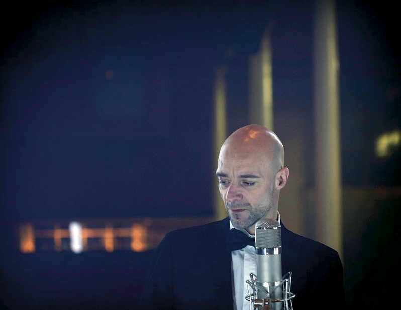 En skaldet mand i smoking, der optræder til Hædersprisfesten 2021, lidenskabeligt syngende i en mikrofon.