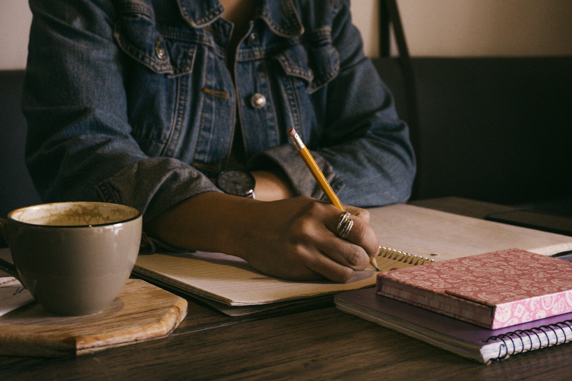 En kvinde skriver i en notesbog, mens hun nyder en kop kaffe.