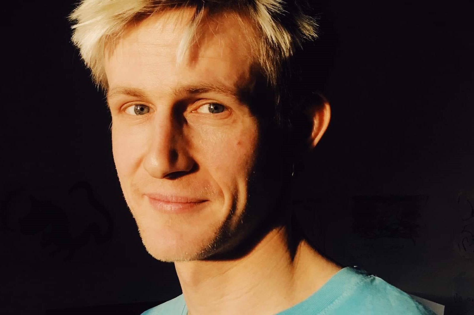 Asger Nordtorp Pedersen, en mand med lyst hår, smiler foran en mørk baggrund.