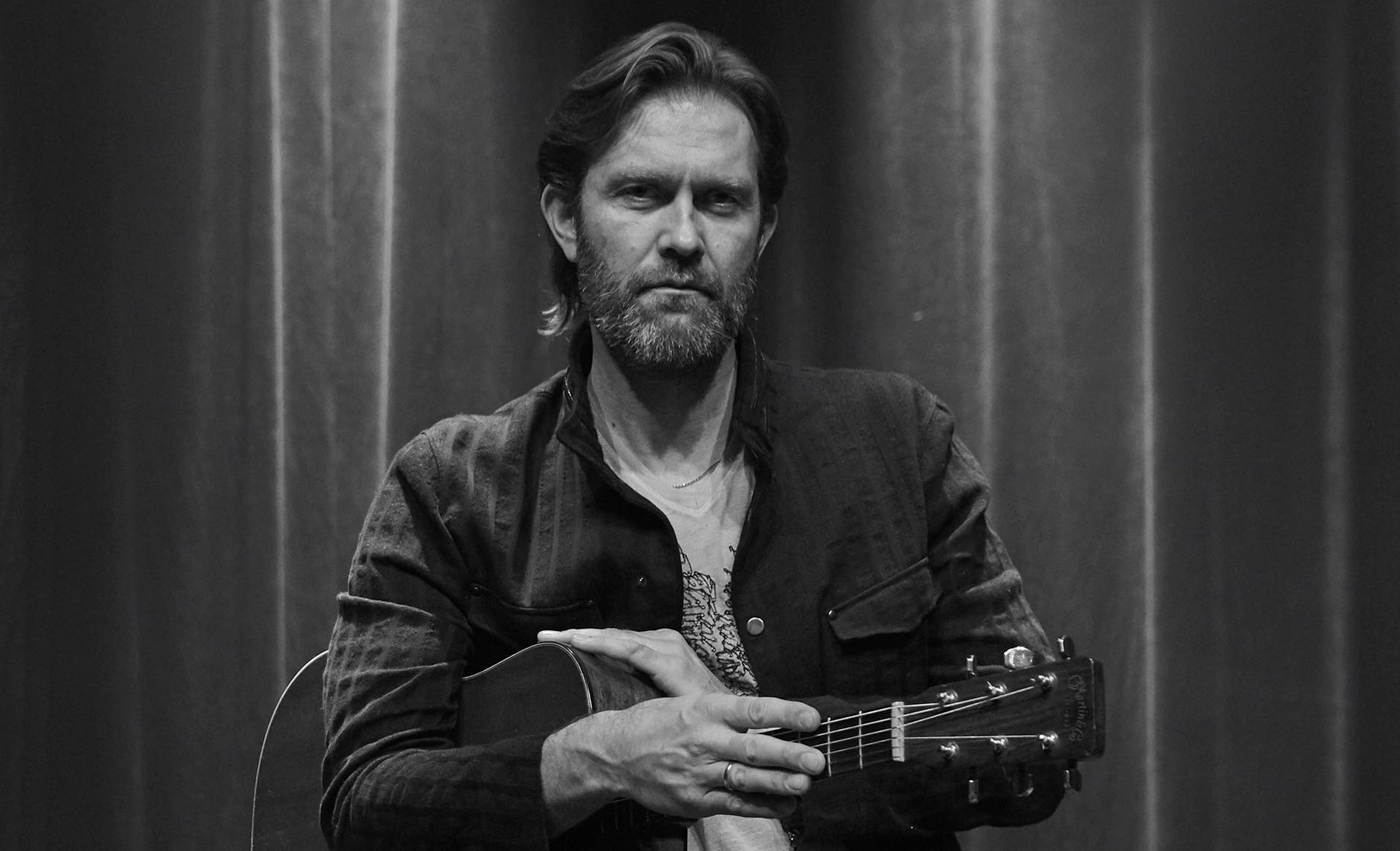 Et sort/hvidt foto af Mike Andersen med en akustisk guitar ved et Netværksaften-arrangement.