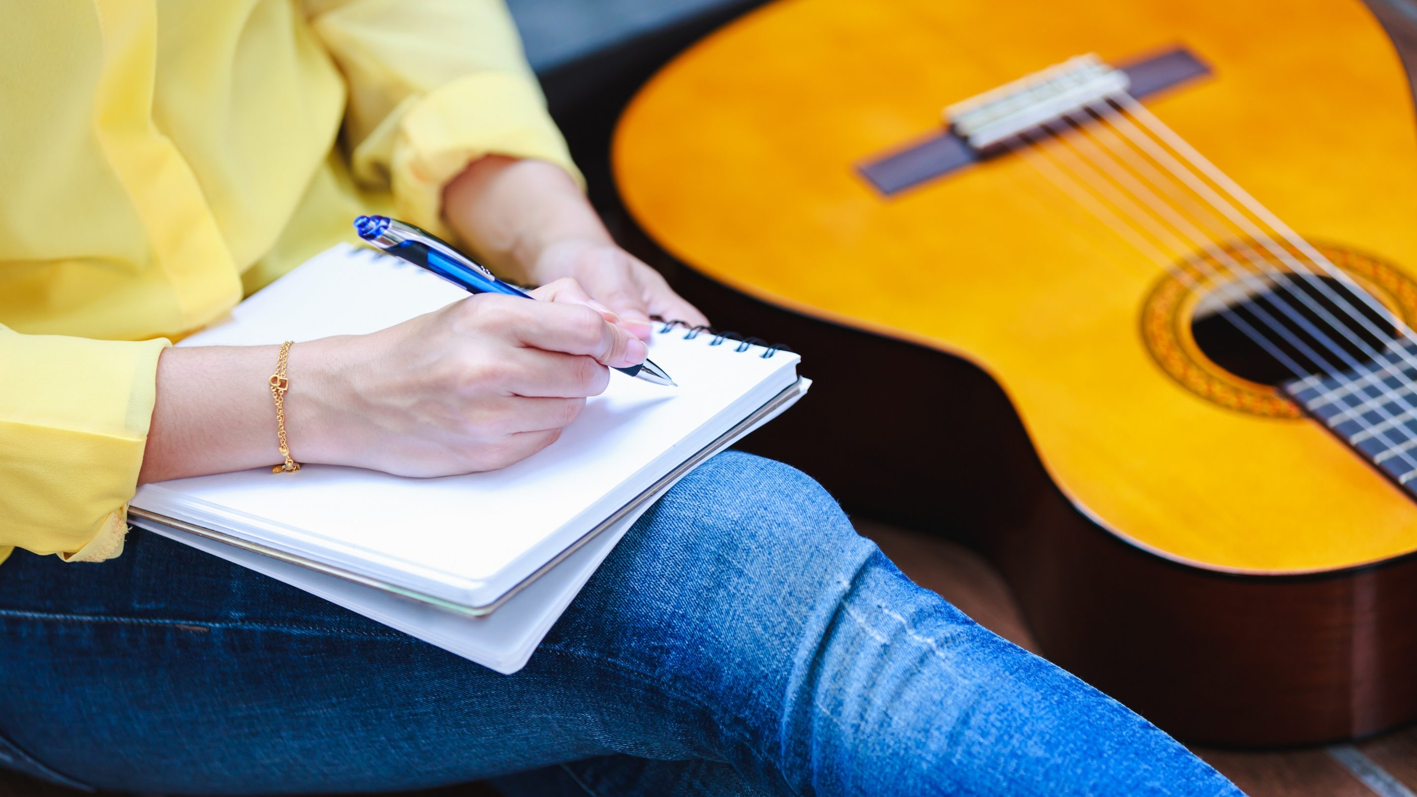En kvinde, der engagerer sig i online-snak, mens hun skriver på en notesbog ved siden af en akustisk guitar, ved at bruge PR og fortælleteknikker.
