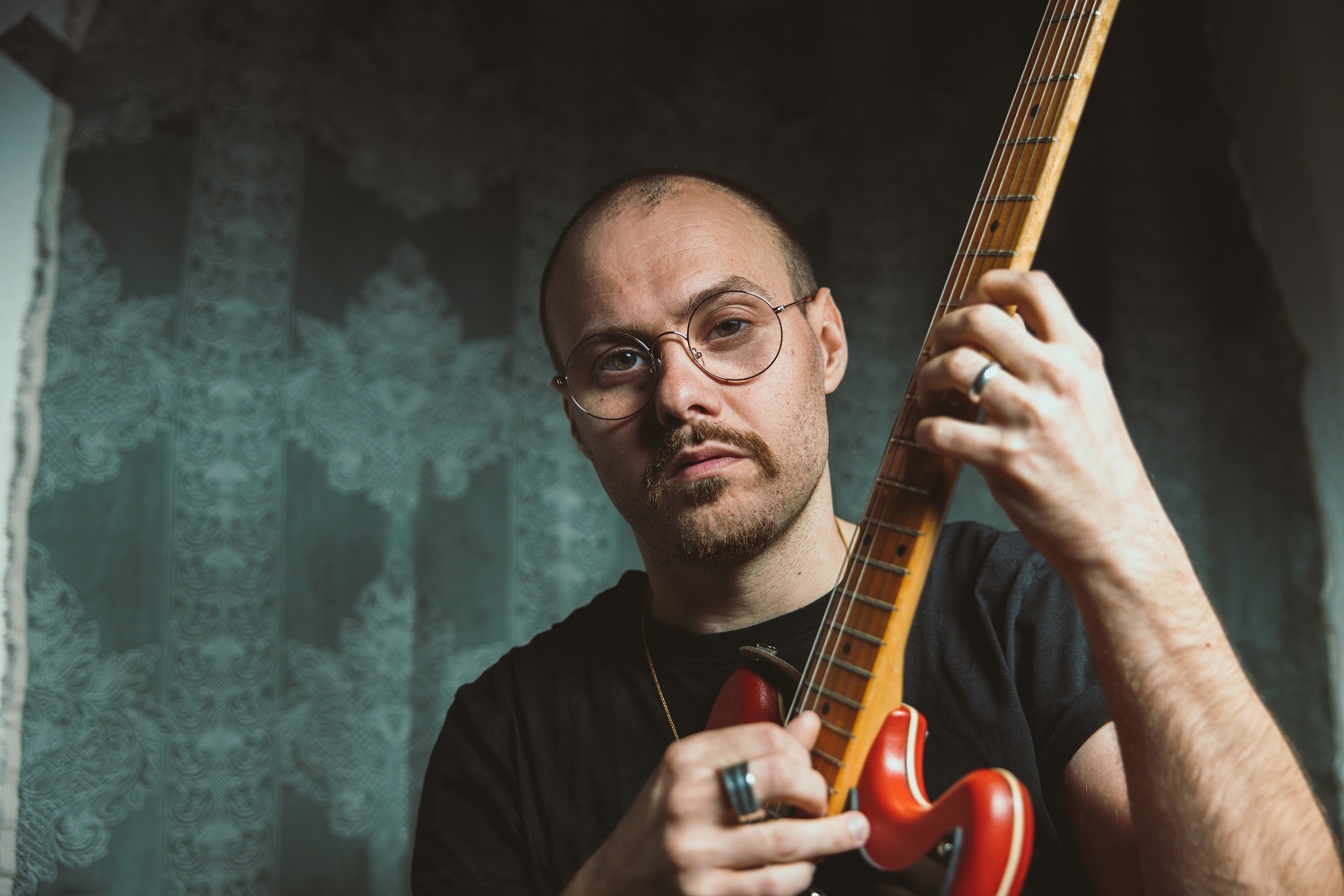 En mand med briller spiller en rød elektrisk guitar.