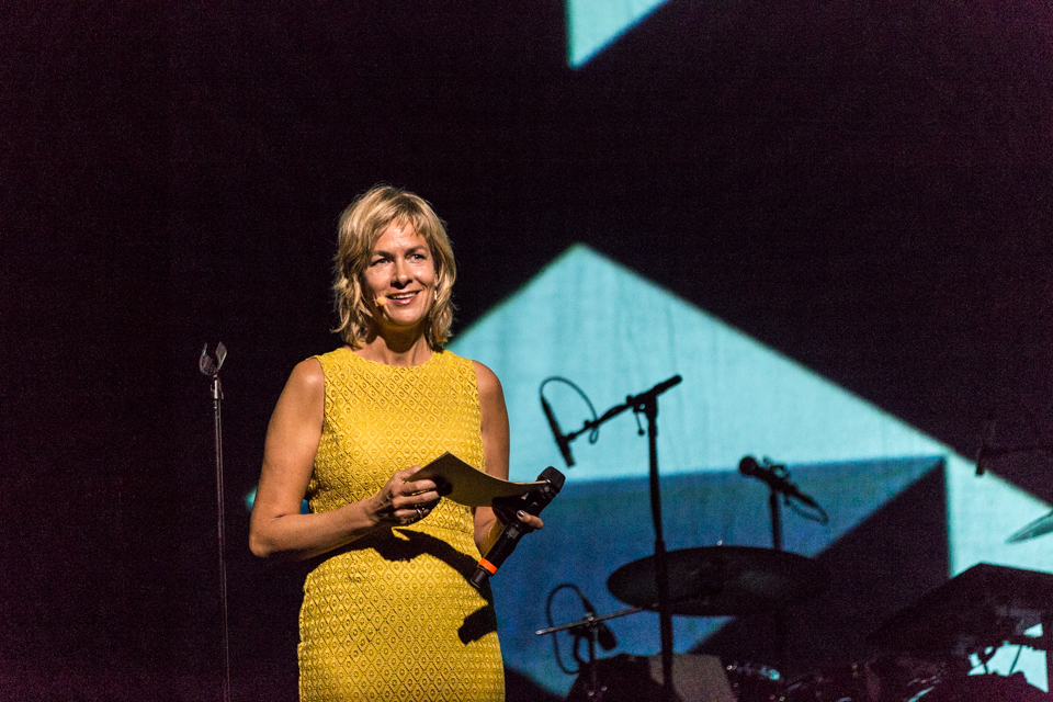 Susi Hyldgaard, en kvinde i gul kjole, står på scenen.
