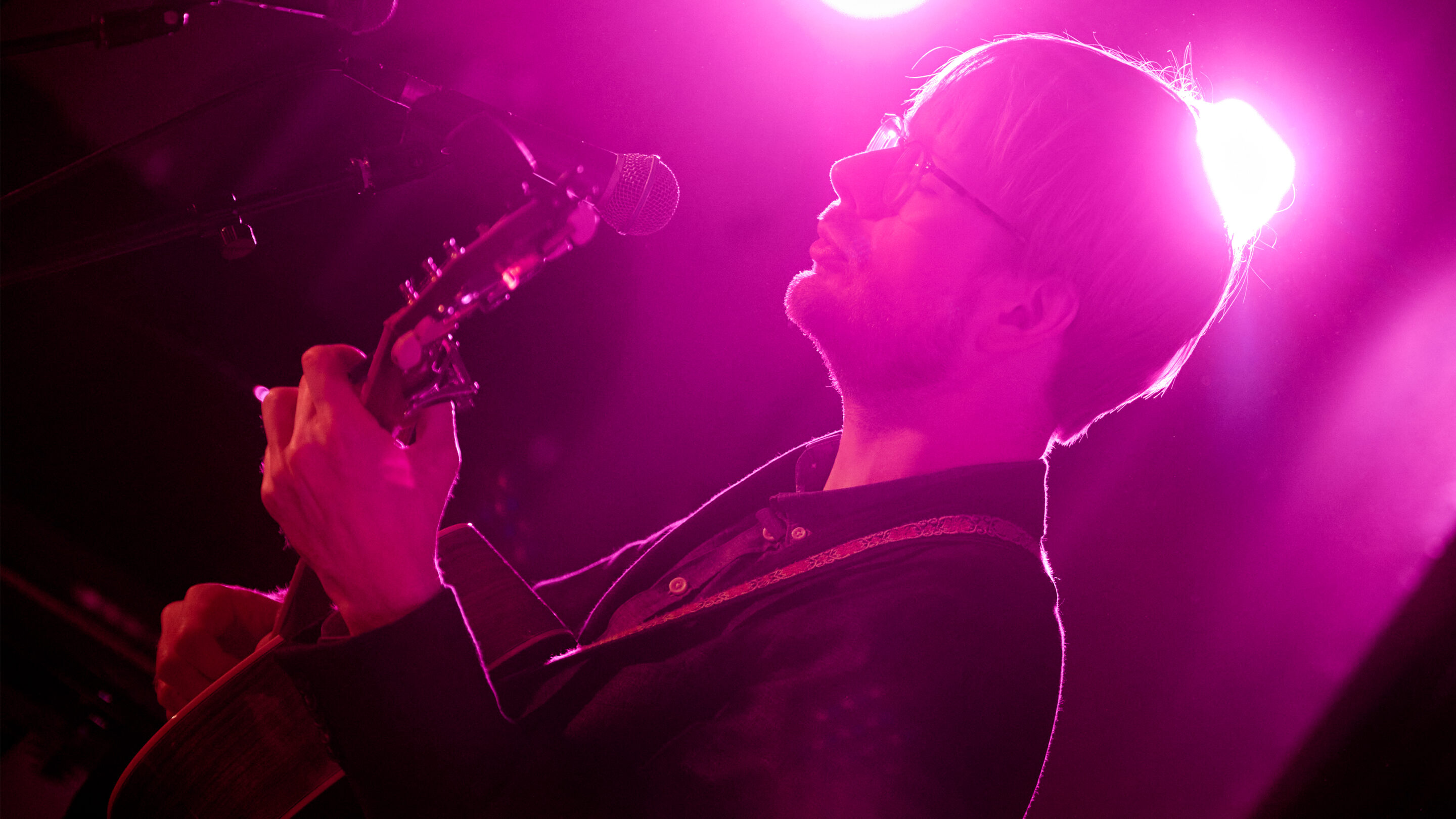 Søren Lyhne, en talentfuld singer-songwriter fra Skabertrang Aarhus, viser sine musikalske evner, mens han lidenskabeligt spiller en akustisk guitar foran en fascinerende pink
