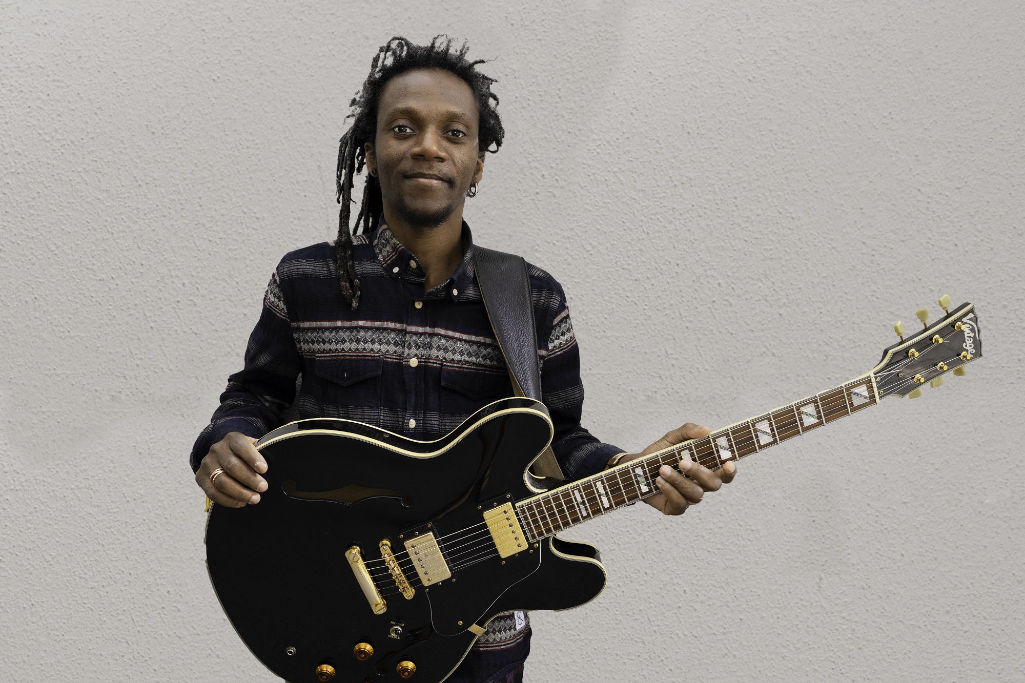 Alain Apaloo, en mand med dreadlocks, der holder en sort elektrisk guitar.