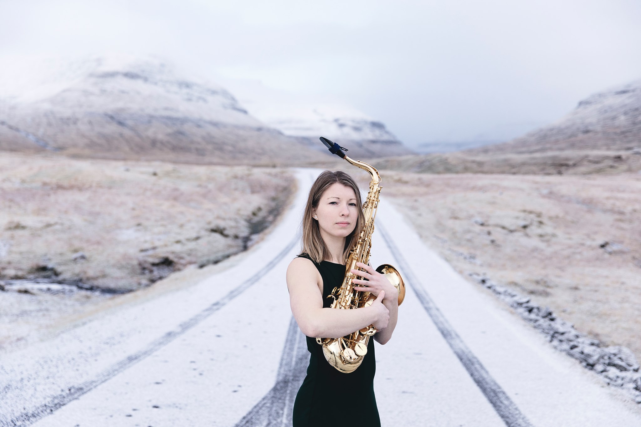 En kvinde, der holder en saxofon på en snedækket vej, viser sine evner som en talentfuld musikkomponist.