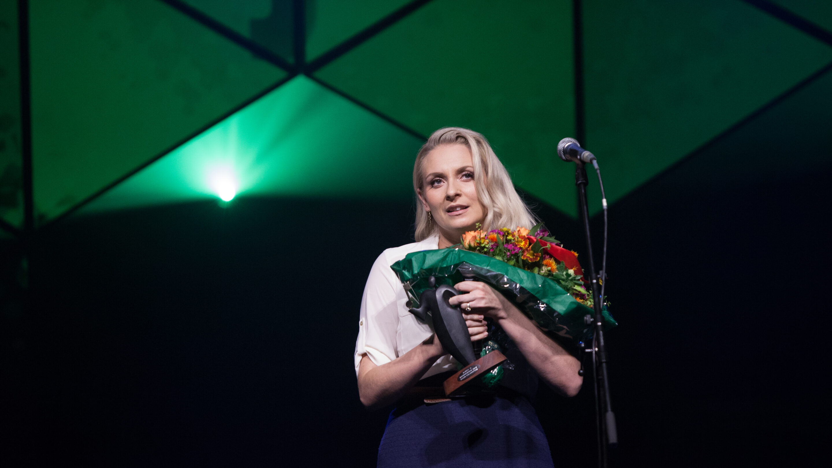 En kvinde holder en buket blomster på scenen til Autors hæderspriser 2024, hvor hun er nomineret.