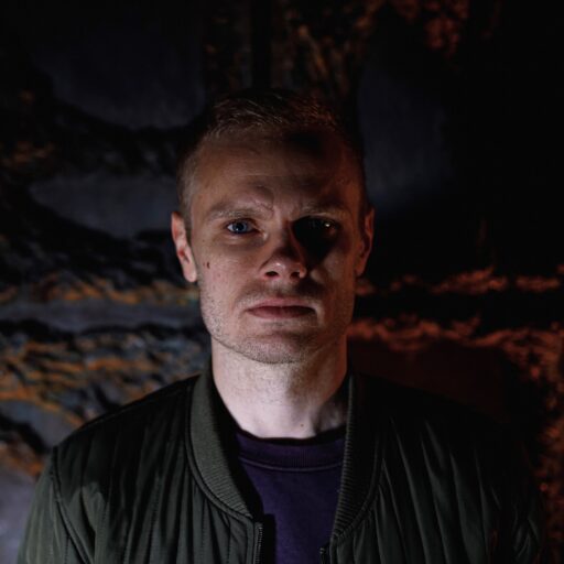 Lars Bork Andersen, en mand i grøn jakke, stående foran en mørk væg.