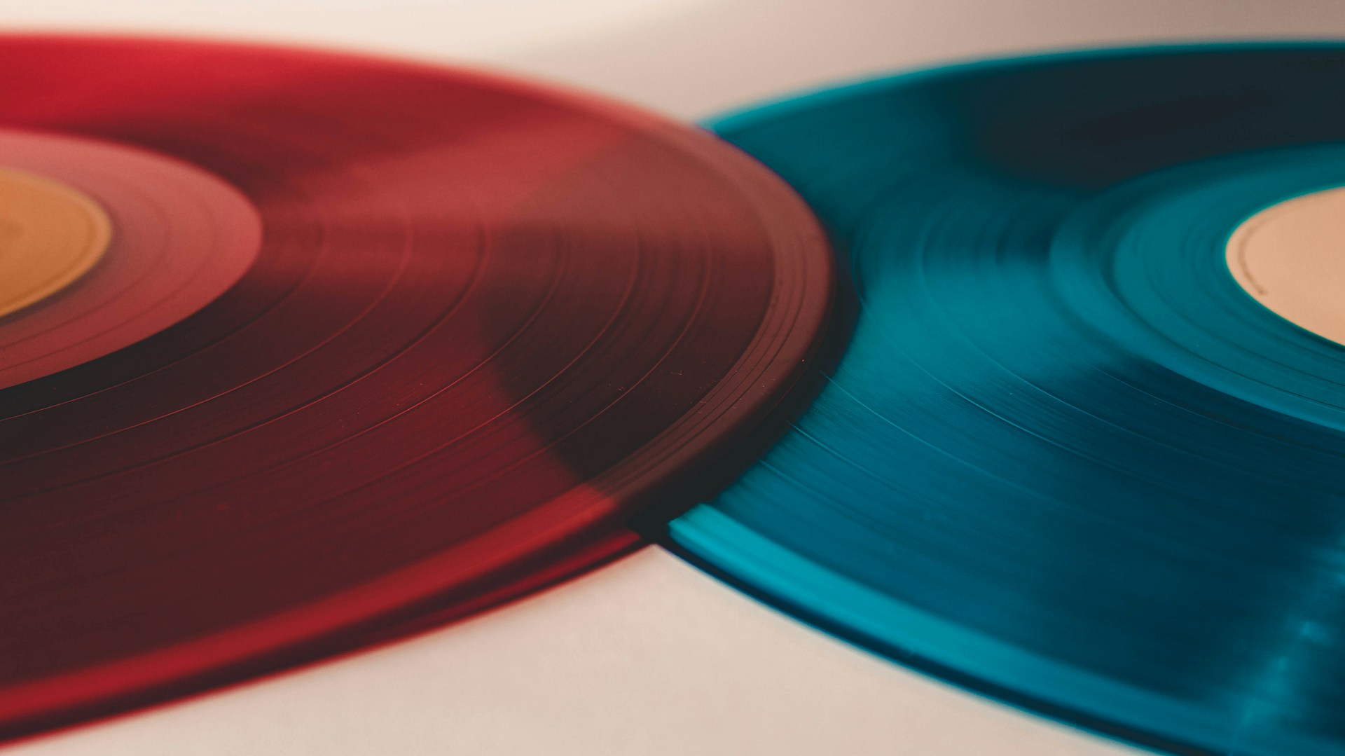 To vinylplader, en rød og en blå, overlappende på en hvid overflade, med fokus på deres teksturerede riller og automatisk kladde.