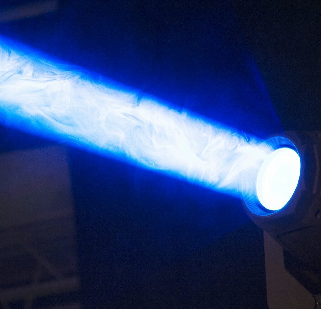 Et scenelys med høj intensitet, der udsender en fokuseret stråle af blåt lys med synlig hvirvlende røg i strålen.