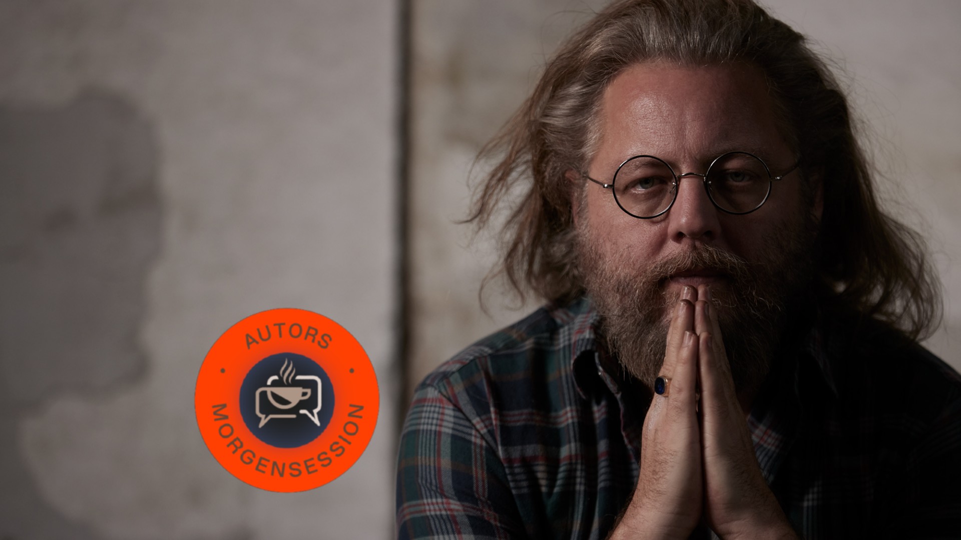 En mand med langt hår, briller og skæg sidder med hænderne presset sammen i tanker; et cirkulært "Autors Morgensession"-logo står ved siden af ham.