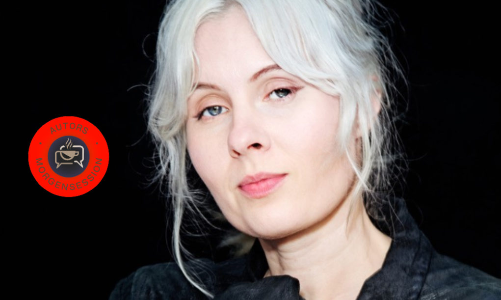 En person med lys hud og hvidt hår, iført en sort skjorte, poserer foran en sort baggrund. Til venstre ses et rødt, cirkelformet logo med en kaffekop og tysk tekst.