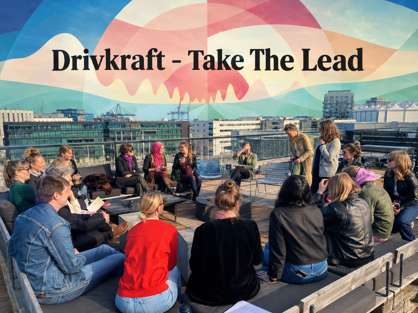 En gruppe mennesker sidder i en halvcirkel på en tagterrasse og lytter til en taler. I baggrunden ses byens bygninger og et vægmaleri med teksten »Drivkraft – Take The Lead«.